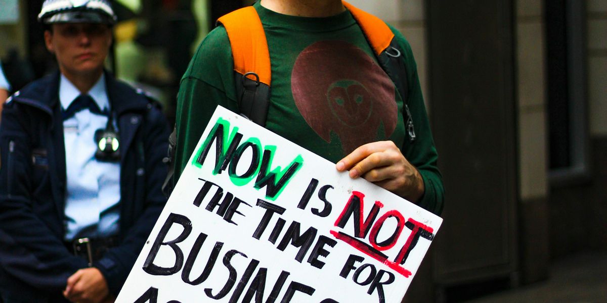 Man holding sign that says Not is not the time for business as usual; climate action now.