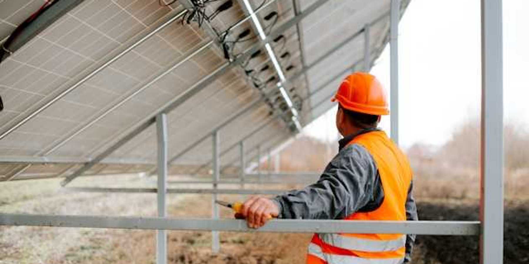 Man in an orange safety vest standing under a solar panel