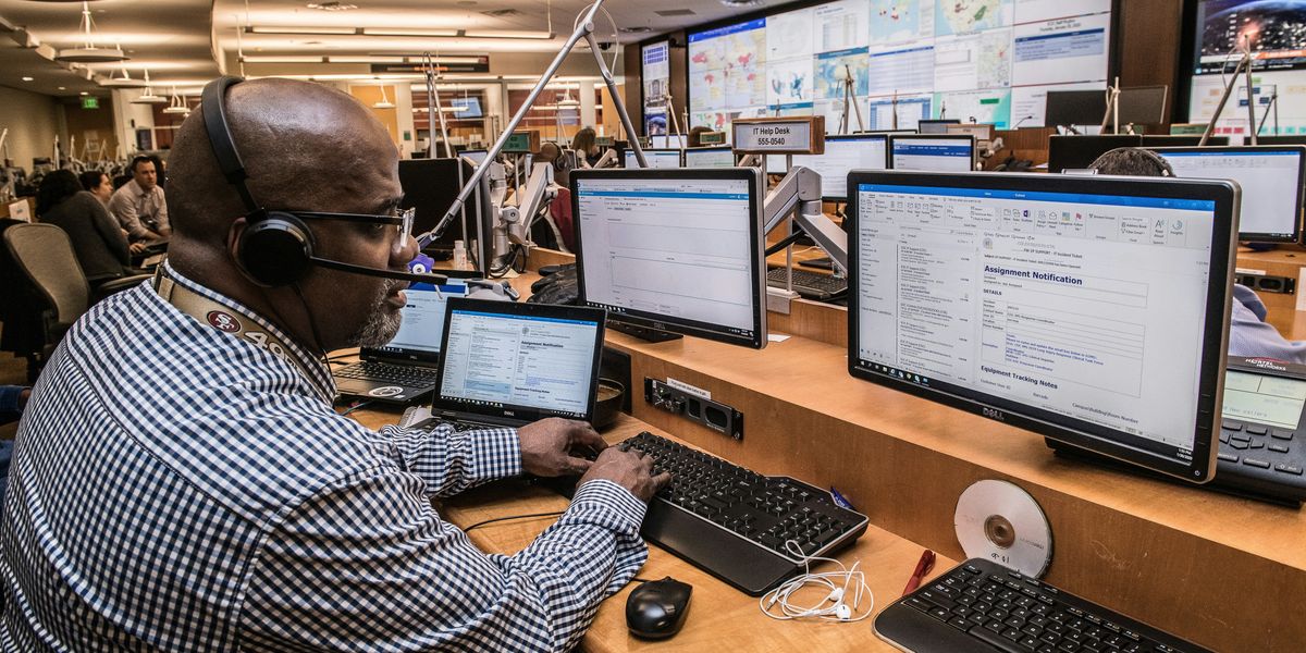 man in black and white checkered dress shirt using computer in a command center.