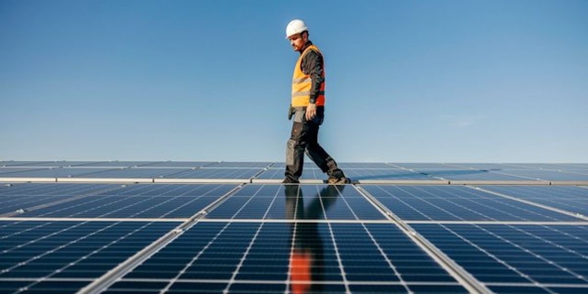 Man in safety vest and hard hat walking between solar panels.