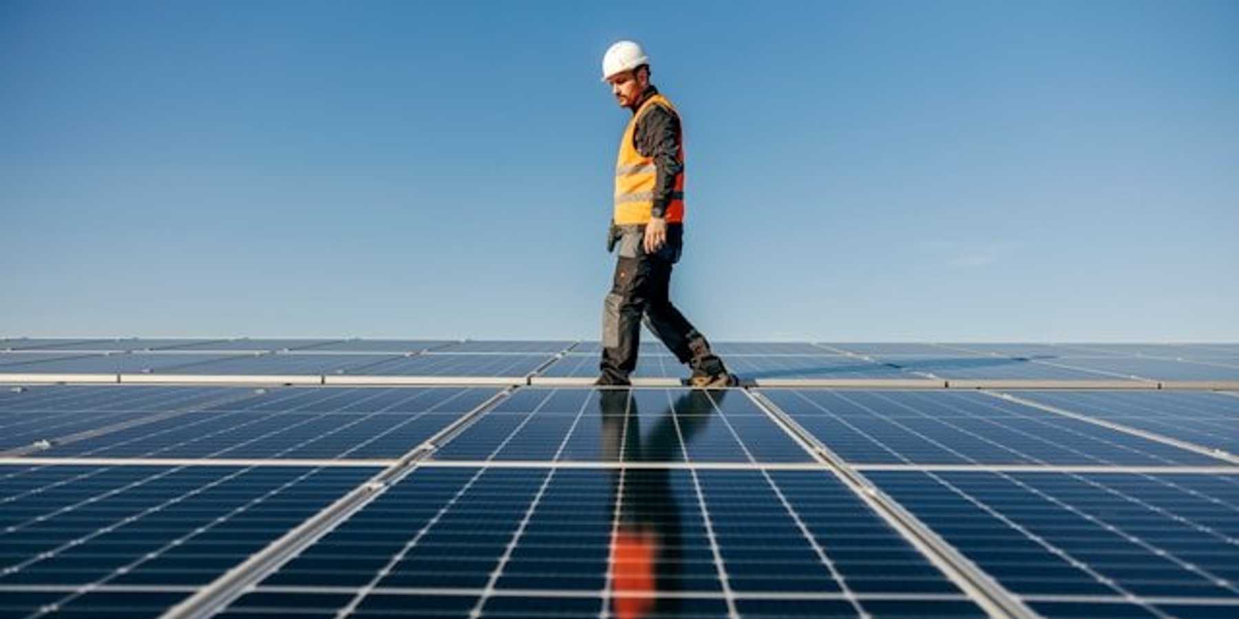 Man in safety vest and hard hat walking between solar panels.