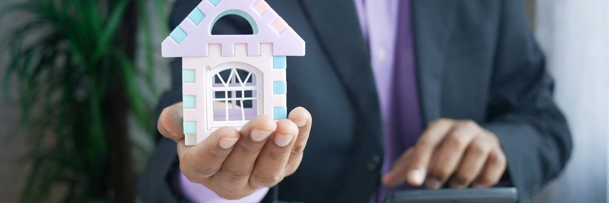 man in suit holding a toy model of a house and using a calculator
