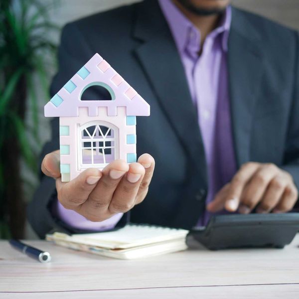 man in suit holding a toy model of a house and using a calculator