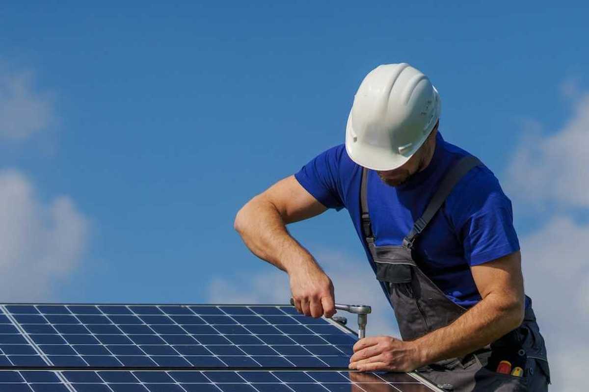 Man in white hard hat and blue shirt installing solar panels
