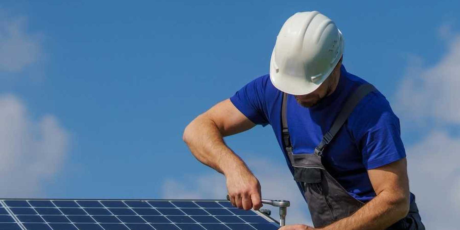 Man in white hard hat and blue shirt installing solar panels