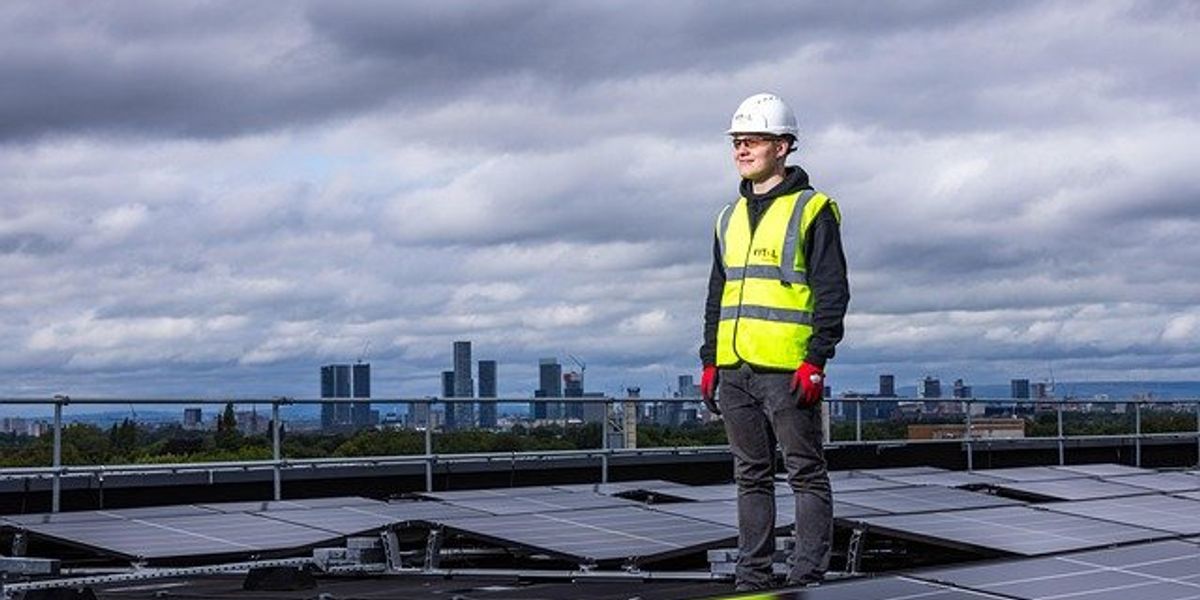 Man in yellow safety vest and hard hat standing on a roof with solar panels.