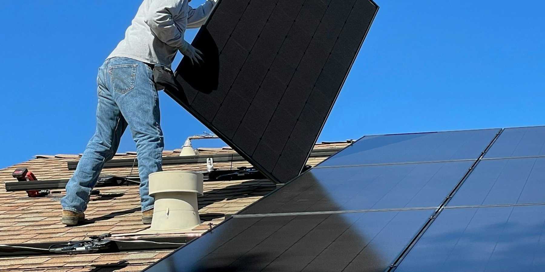Man installing solar panels on house roof.