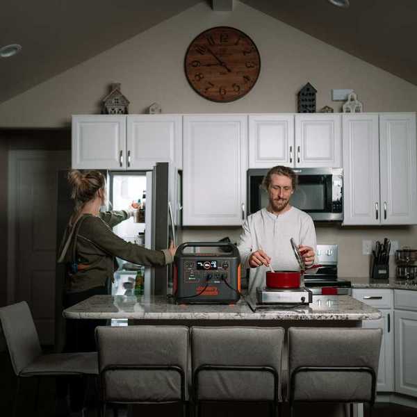 Man prepares dinner in kitchen while woman opens refrigerator during power outage while appliances are powered by a portable power station.