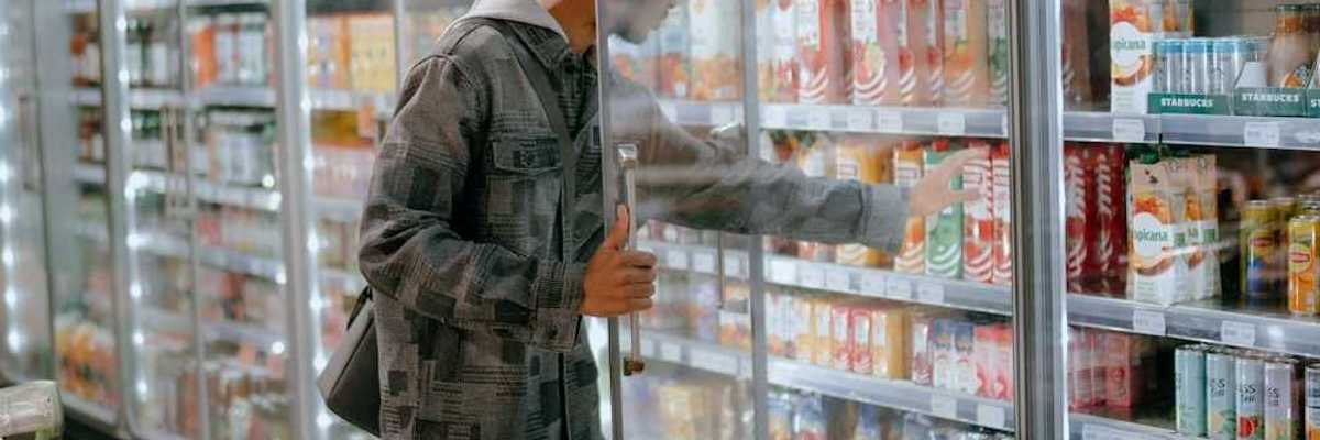 Man reaching into a supermarket refrigeration cooler for a carton of milk