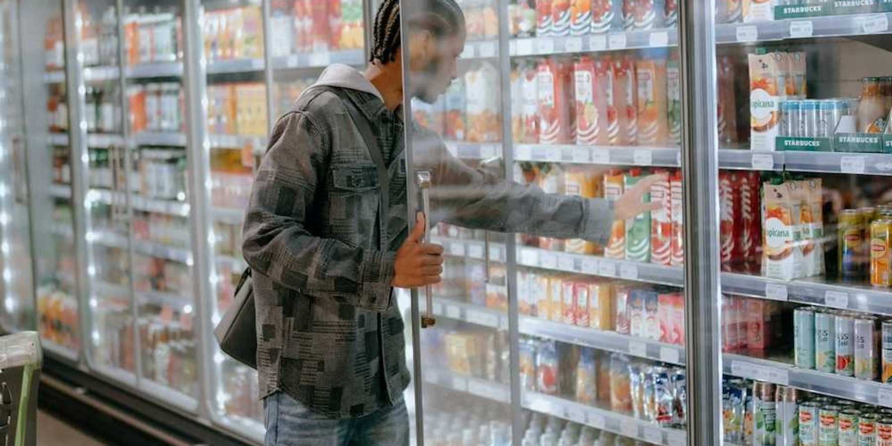 Man reaching into a supermarket refrigeration cooler for a carton of milk