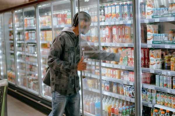 Man reaching into a supermarket refrigeration cooler for a carton of milk