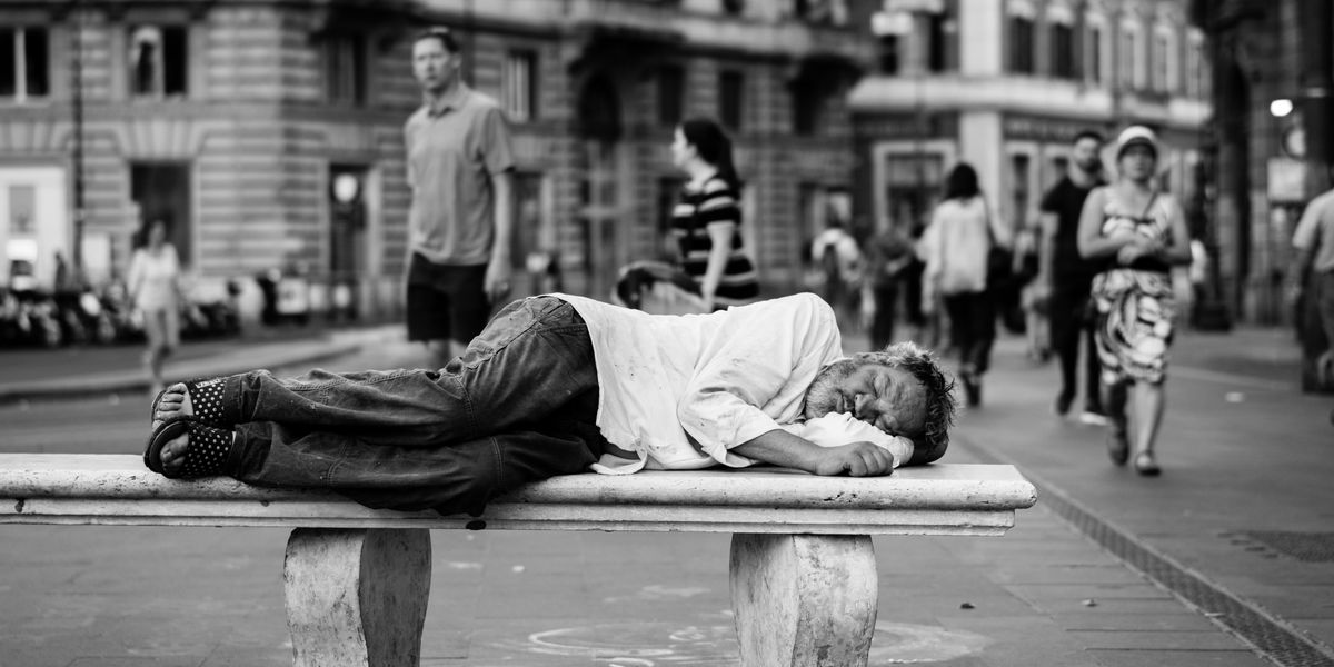 man sleeping on bench in the middle of the street.