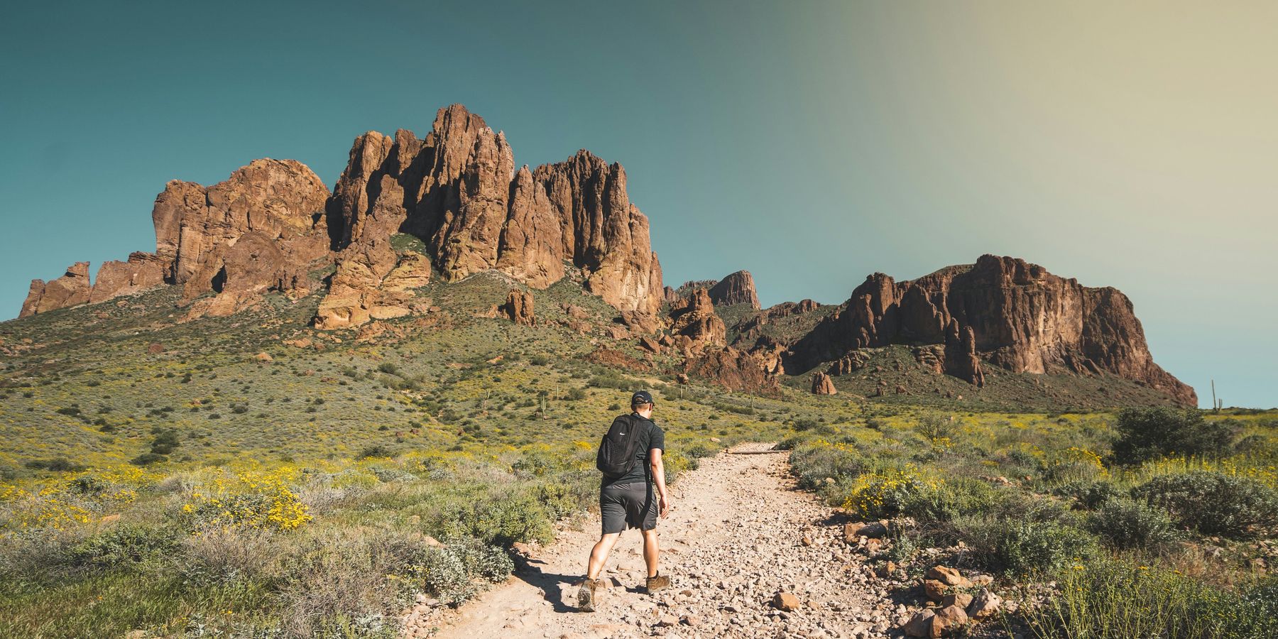man walking up towards hill in dry, rocky desert environment.