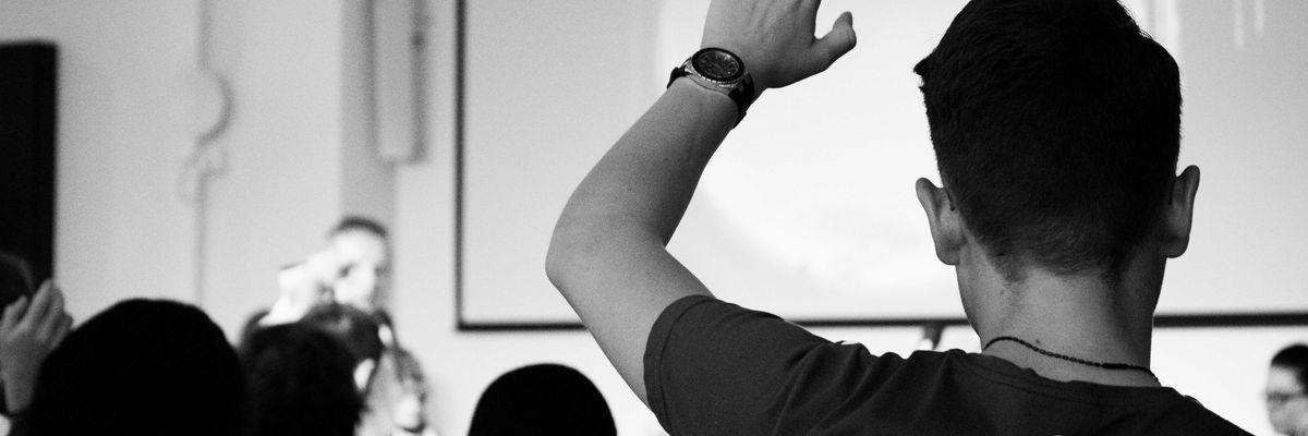 man wearing black t-shirt close-up photography raising his hand in a college classroom