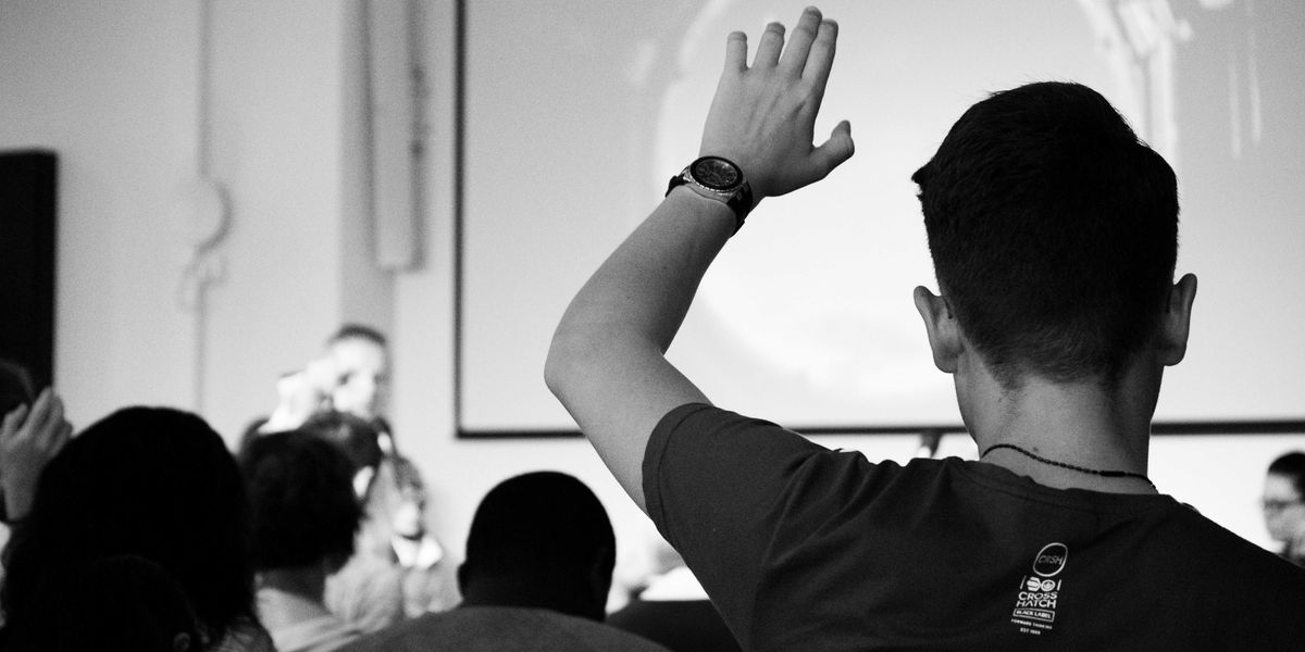 man wearing black t-shirt close-up photography raising his hand in a college classroom