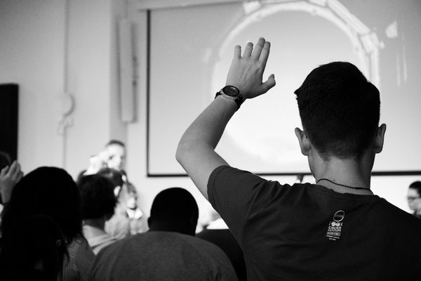 man wearing black t-shirt close-up photography raising his hand in a college classroom
