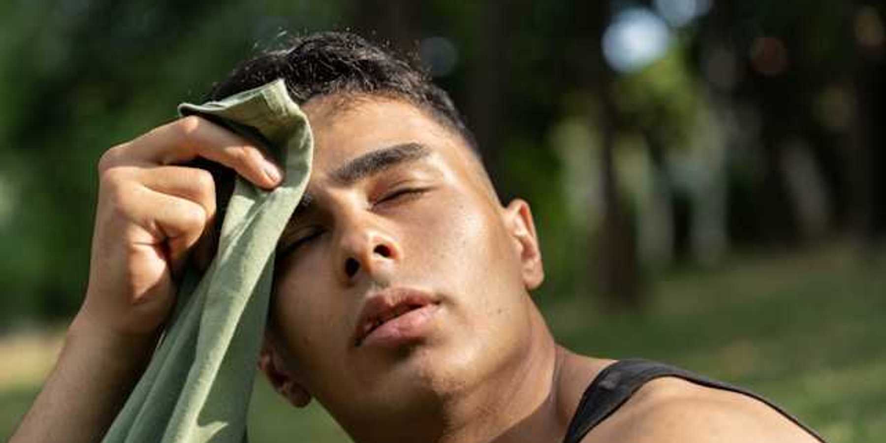 Man wiping the sweat off of his forehead with a shirt while sitting outside in a park