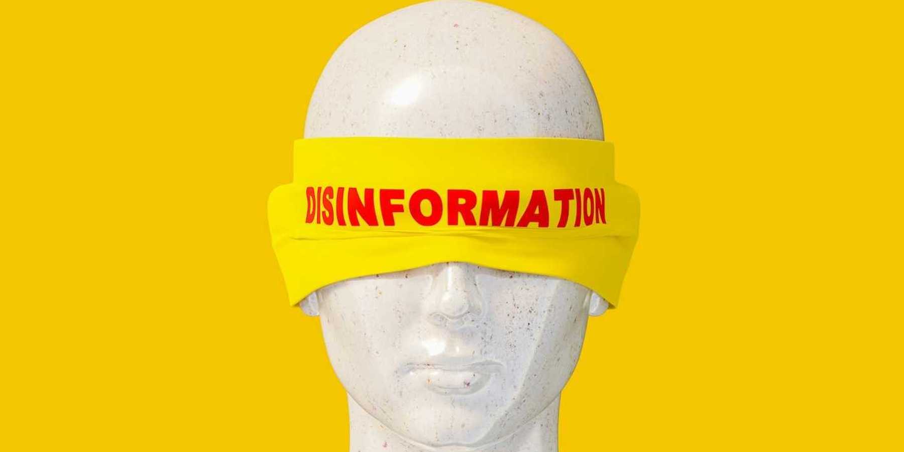 Mannequin head shot wearing a yellow blindfold labeled "disinformation" in red letters.