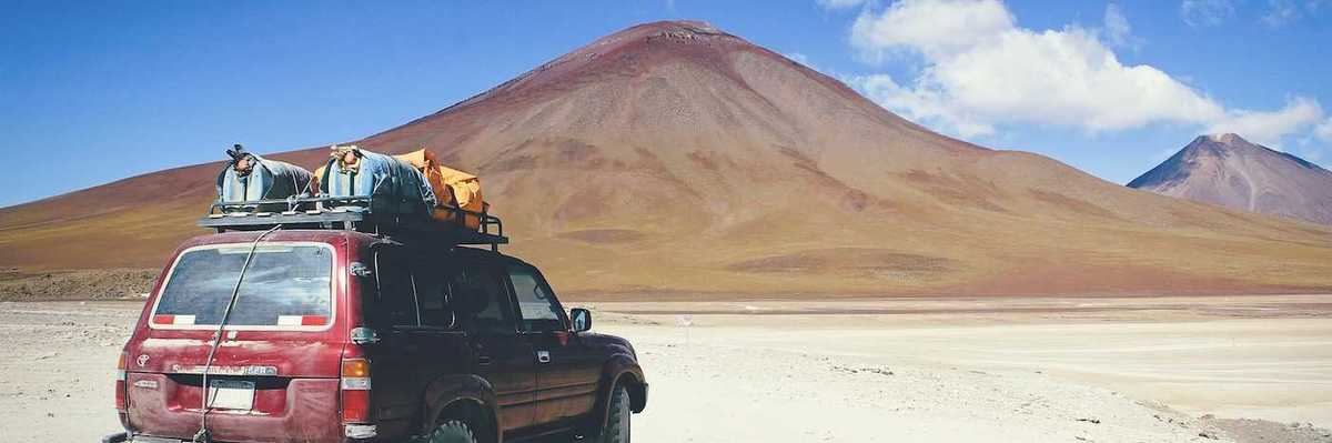 Maroon SUV with baggage on roof rack facing mountains in Bolivian outback