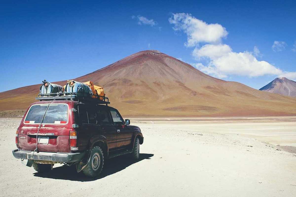 Maroon SUV with baggage on roof rack facing mountains in Bolivian outback