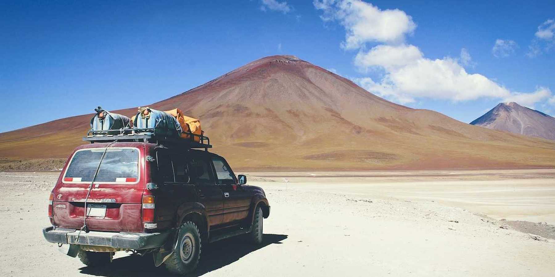 Maroon SUV with baggage on roof rack facing mountains in Bolivian outback