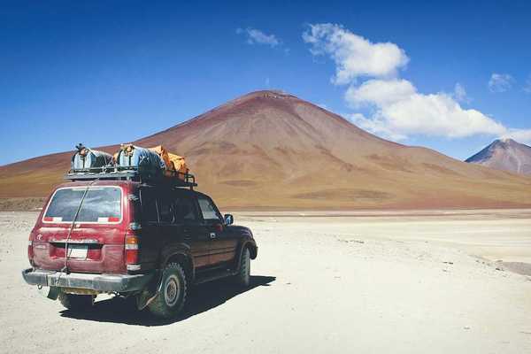 Maroon SUV with baggage on roof rack facing mountains in Bolivian outback