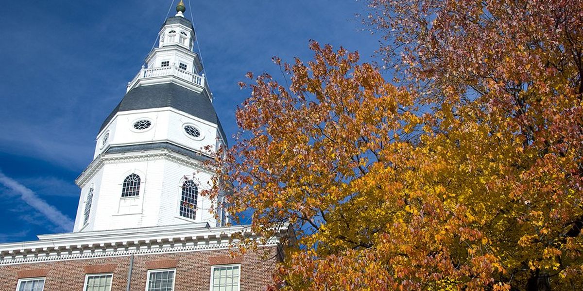 Maryland capitol building with trees showing fall foliage alongside it on a sunny day.