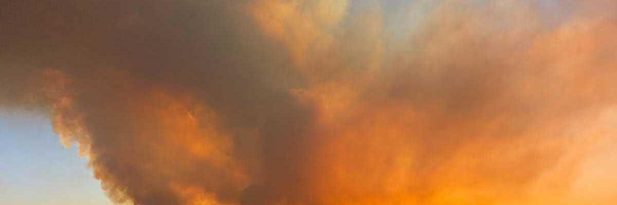 Massive wildfire partially obscuring a setting (or rising sun)