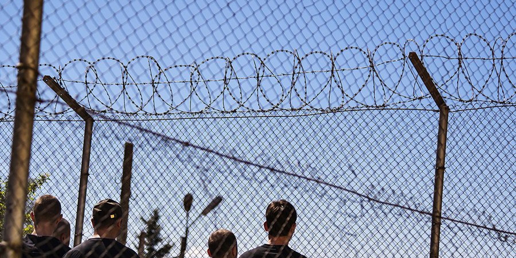 Men standing behind barbed wire fences.