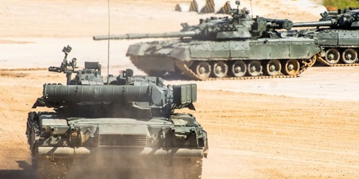 Military tanks driving on a dirt surface.