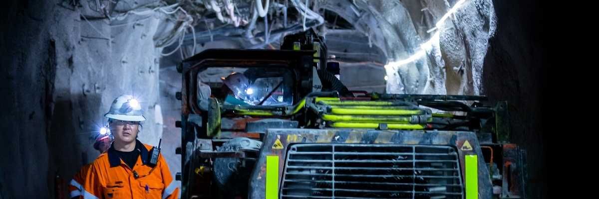 Miner in reflective orange jacket working underground alongside boring machine