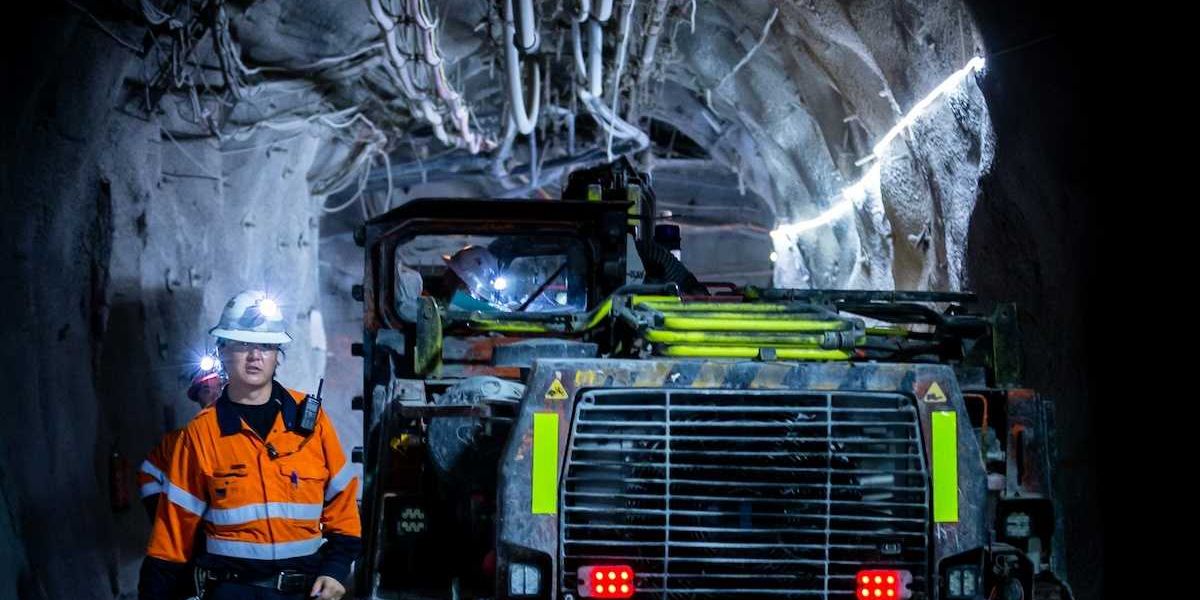 Miner in reflective orange jacket working underground alongside boring machine