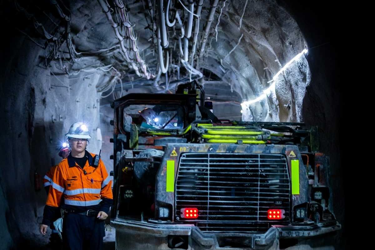 Miner in reflective orange jacket working underground alongside boring machine