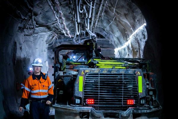 Miner in reflective orange jacket working underground alongside boring machine