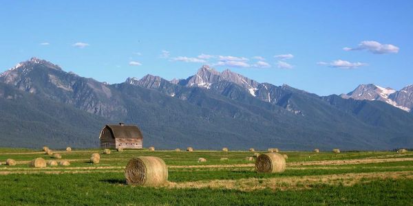 Montana landscape with barn and round-baled hay against snow-capped Rocky Mountains