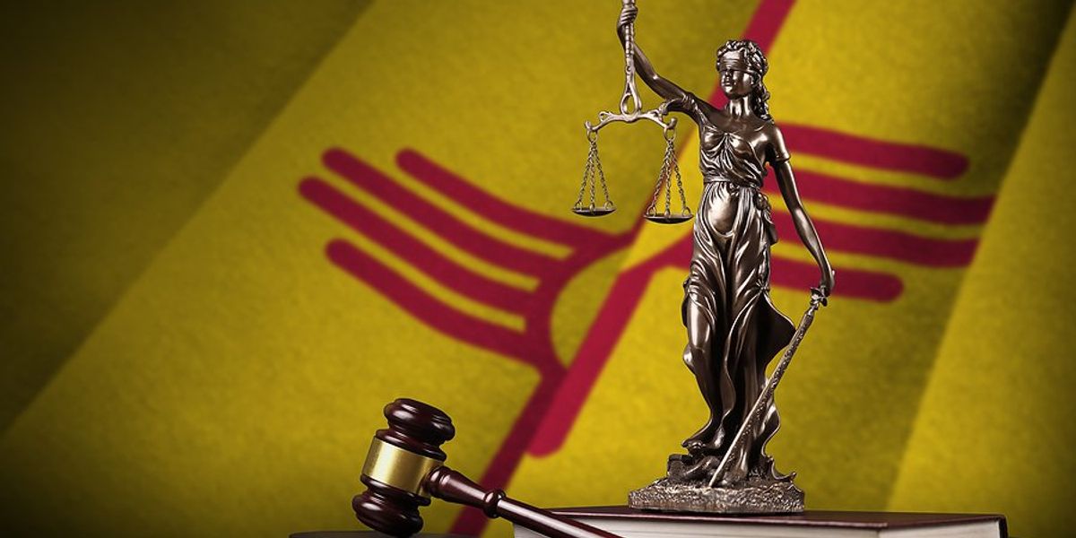 New Mexico state flag with statue of lady justice, constitution and judges gavel on black drapery.