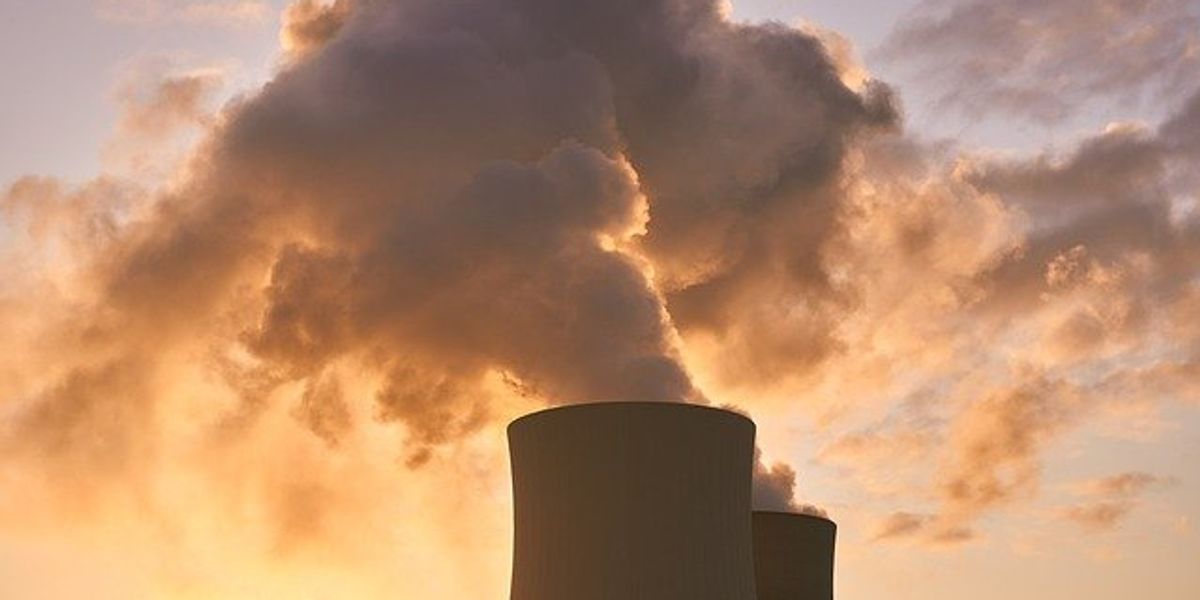 Nuclear power plant with smoke emitting from two towers with sunset sky in background.