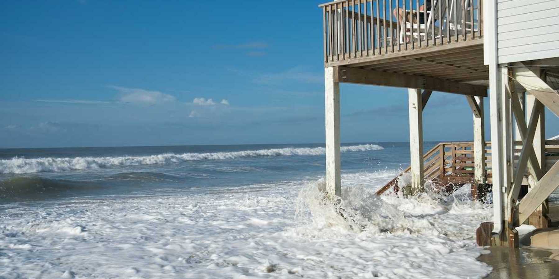 Ocean waves lap against the piers supporting a seaside home
