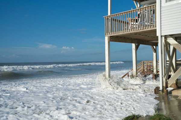 Ocean waves lap against the piers supporting a seaside home