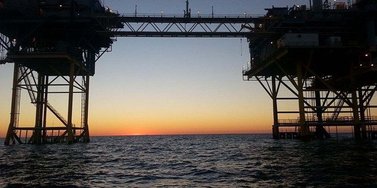 Offshore oil rig silhouetted on the water at sunset.