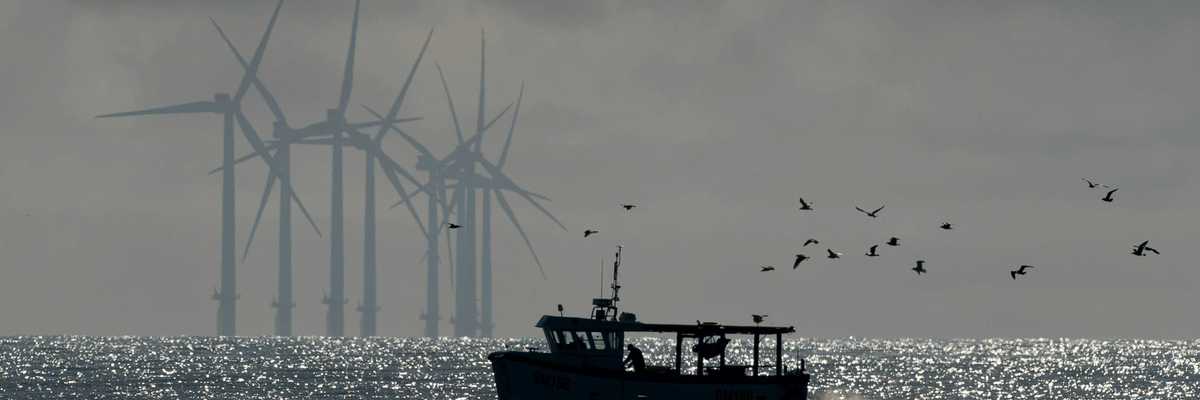 Offshore wind turbines with a fishing boat and birds flying in the foreground.