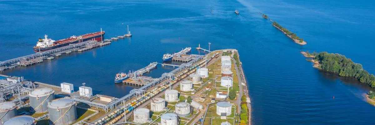 Oil and gas export terminal tanker at dock and multiple storage tanks adjacent to a large waterbody