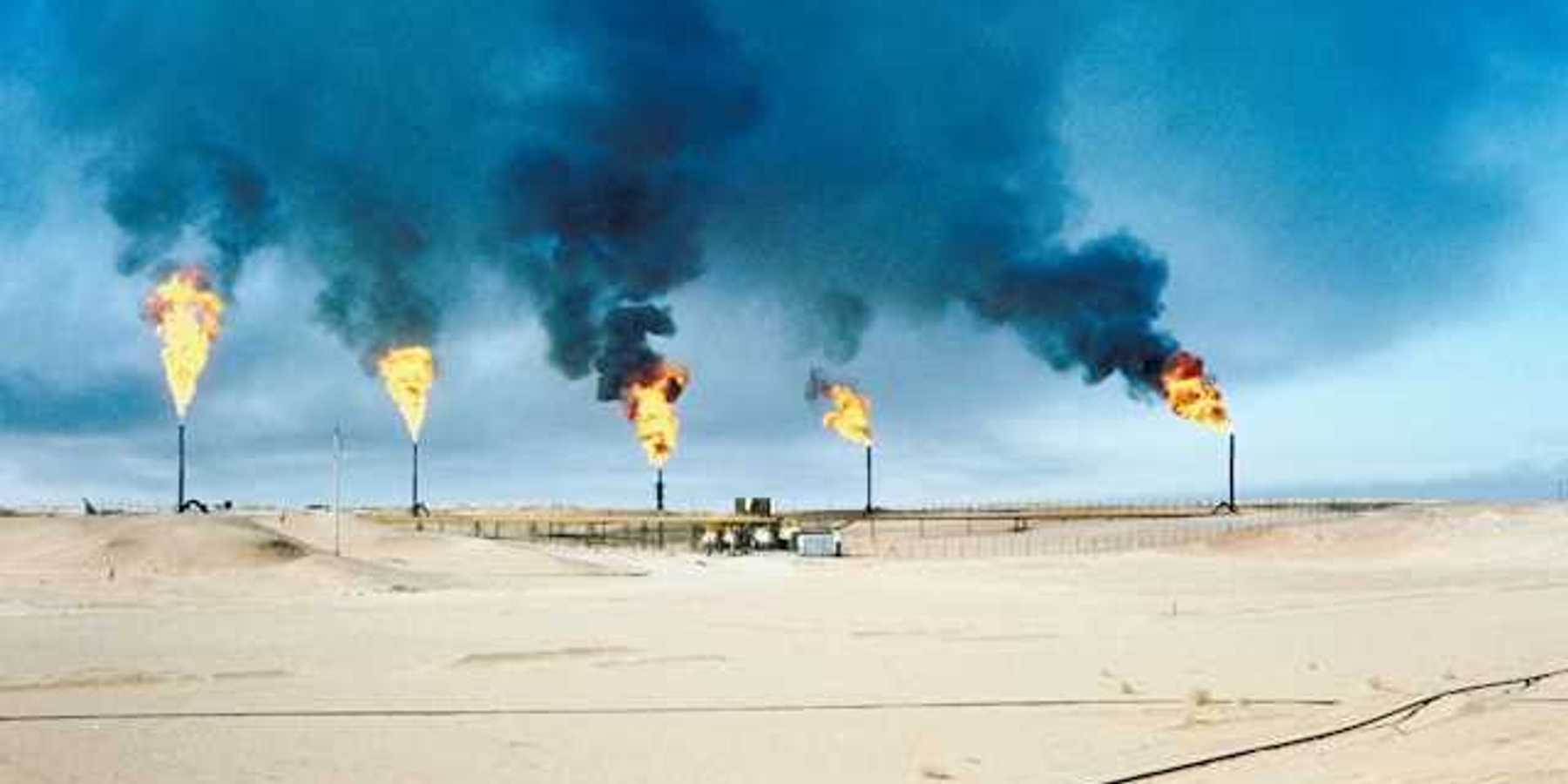 Oil and gas flaring in a desert landscape with black smoke billowing into the sky