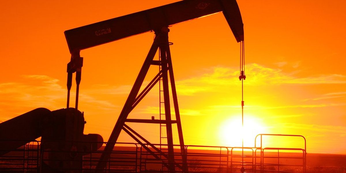 Oil drilling pump jack silhouetted with the sunset in the distance.
