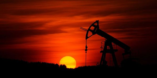 Oil drilling rig silhouetted against a red sunset sky.