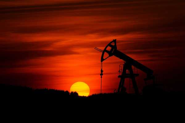 Oil drilling rig silhouetted against a red sunset sky.