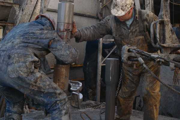 Oil field workers manipulating a drilling rig