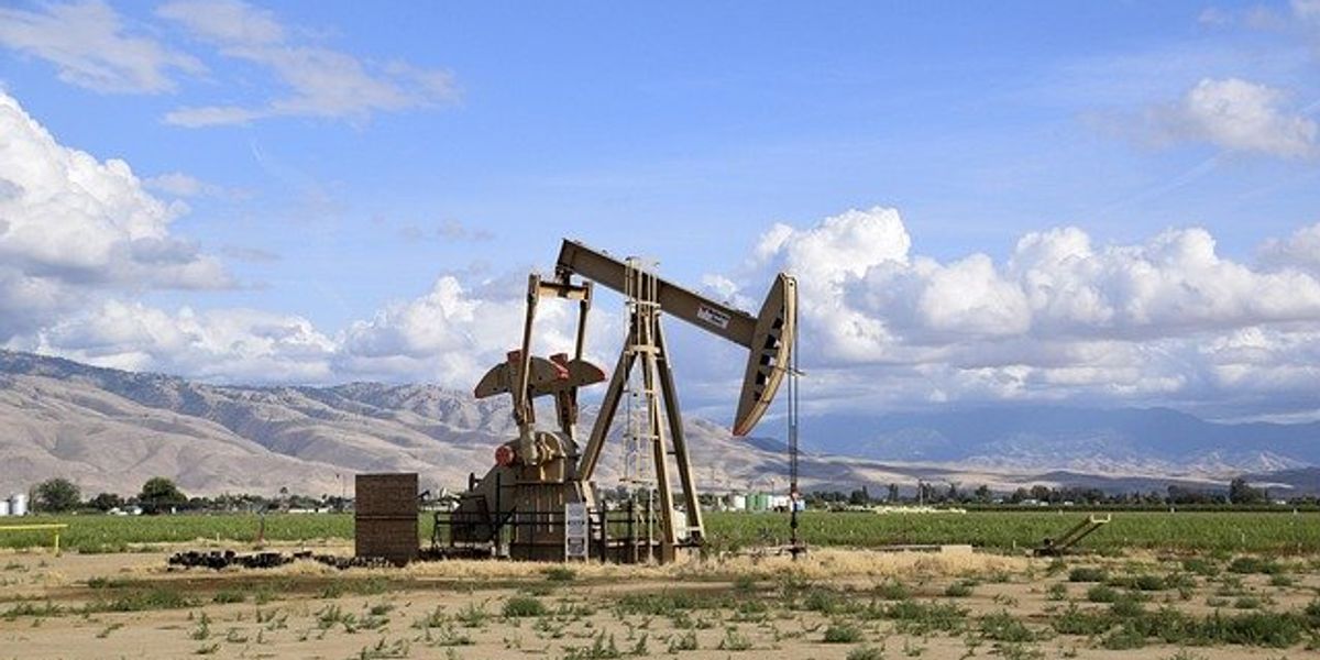 Oil pump jack in front of a field with dry mountains in the background.