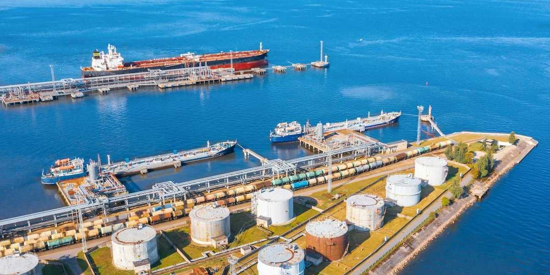 Oil tankers docking at oil terminal adjacent to multiple storage tanks.