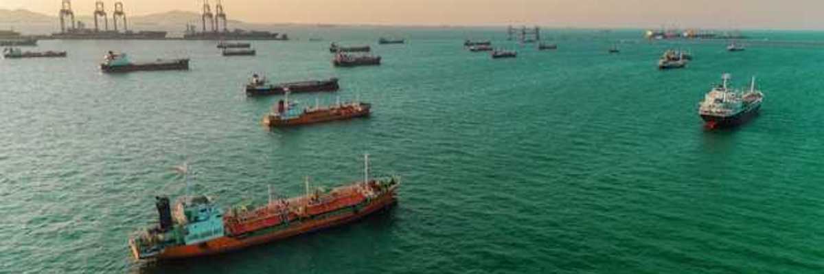 Oil tankers sailing in a bay with a port and docks in the background
